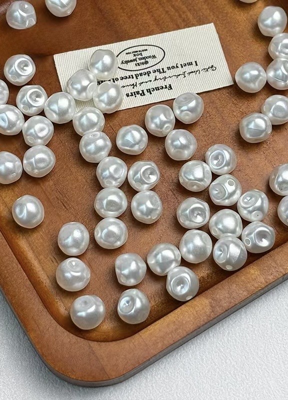 Loose white pearl beads with threading holes arranged on a wooden tray beside a paper label